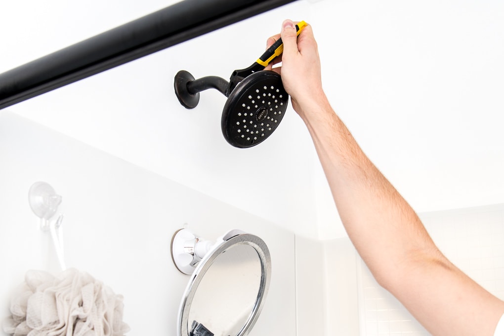 removing an old shower head in a builder grade bathroom