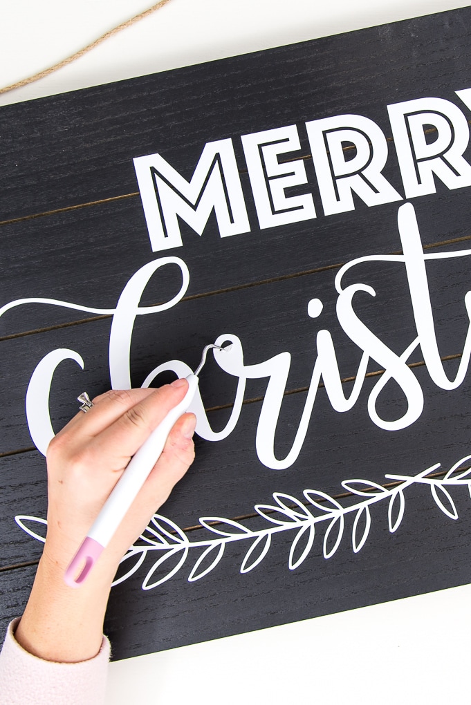 black wooden sign with white vinyl Merry Christmas design weeding detail with weeder tool