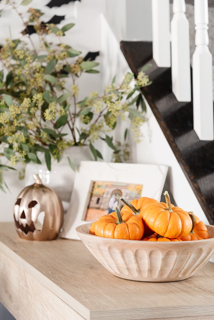 mini pumpkins in a wooden bowl with greenery and pumpkin in the background