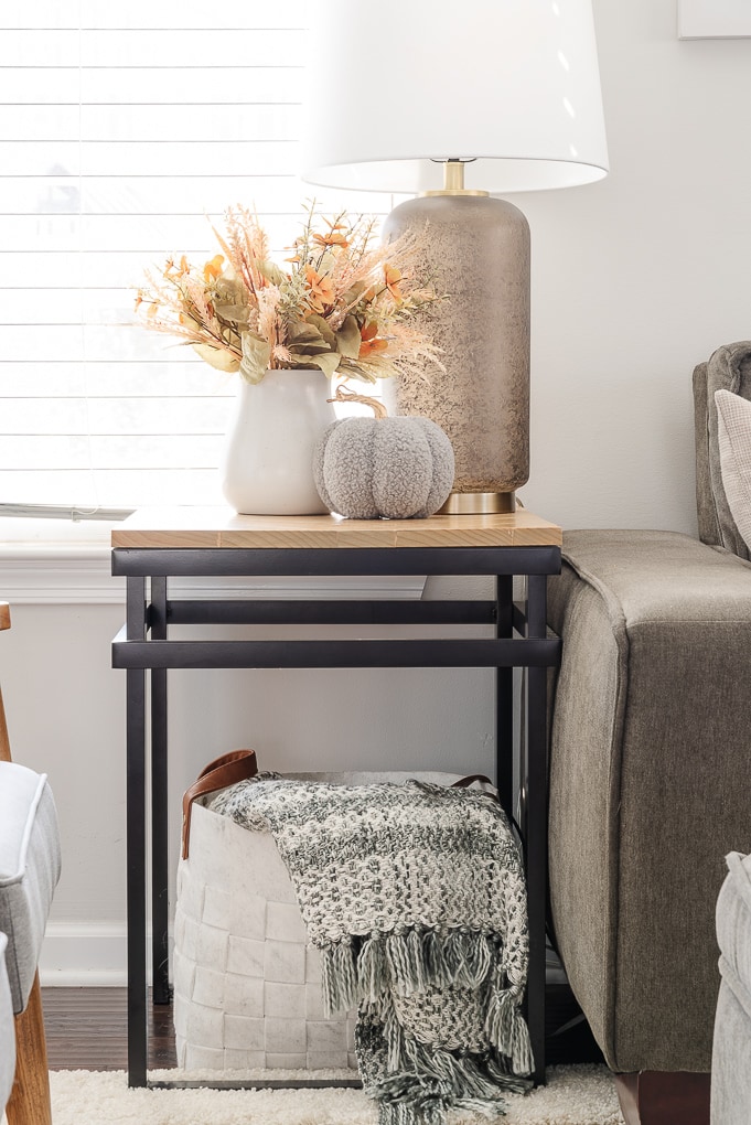 knitted pumpkin and vase of fall florals on end table with throw blanket in a basket