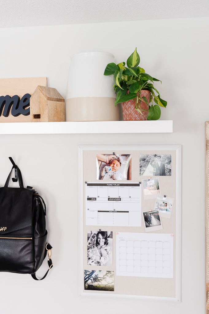 bulletin board with photos and printables and a shelf with a plant