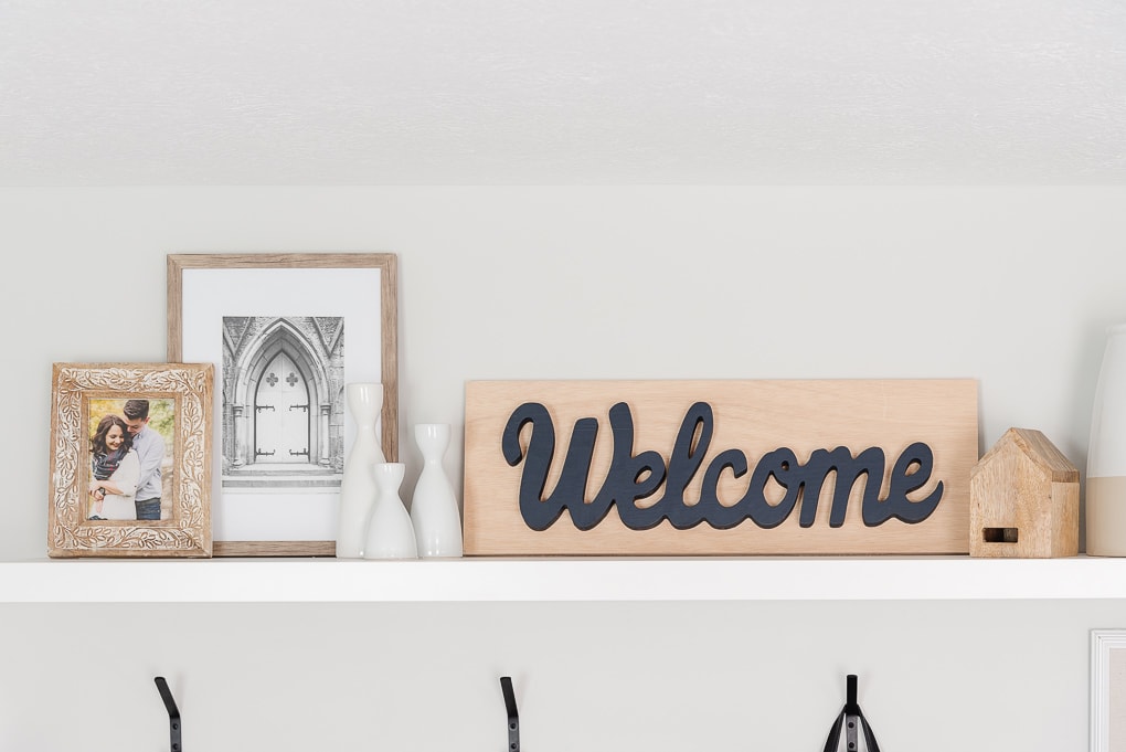 wooden welcome sign in entryway on shelf with other framed decor