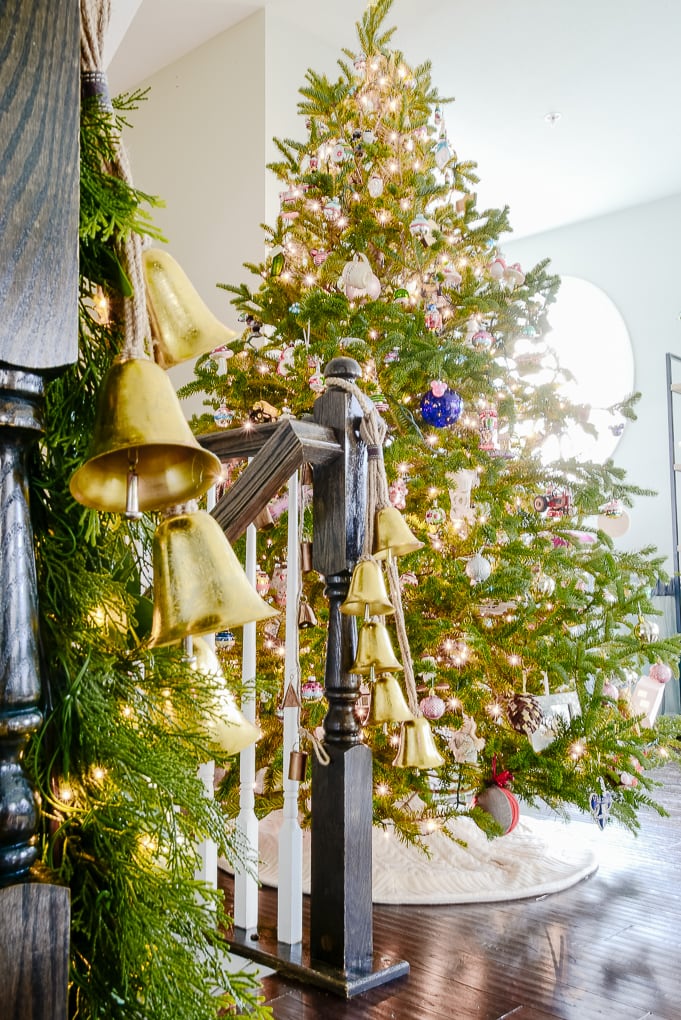 gold hanging bell garlands on staircase by fresh decorated Christmas tree