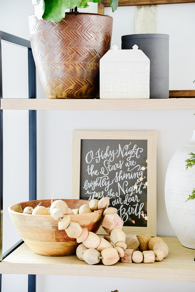 Studio McGee wooden garland from target in wooden bowl on shelf with O Holy Night print framed in the background from Lindsay Letters