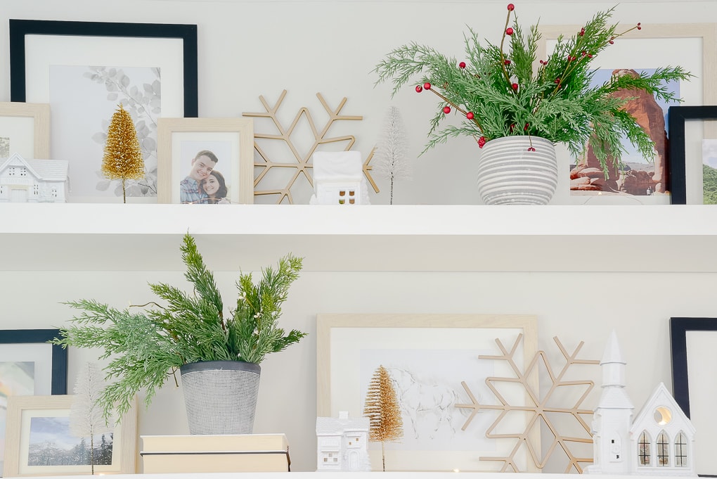 styled shelves decorated for Christmas in living room with white Christmas village houses, gold metal snowflake figurines, and white and gold bottle brush trees