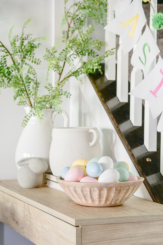 natural wooden bowl filled with eggs on console table and white vases in the background