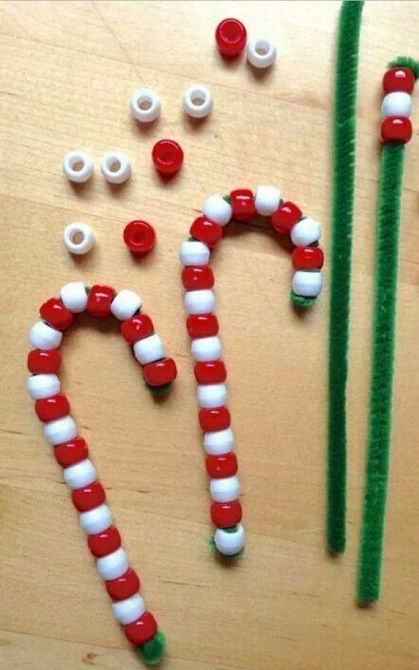 Red and white beads on green pipe cleaners form candy cane shapes on a wooden surface, evoking cherished holiday memories. Extra beads and pipe cleaners are scattered around, perfect for kid-friendly Christmas crafts.