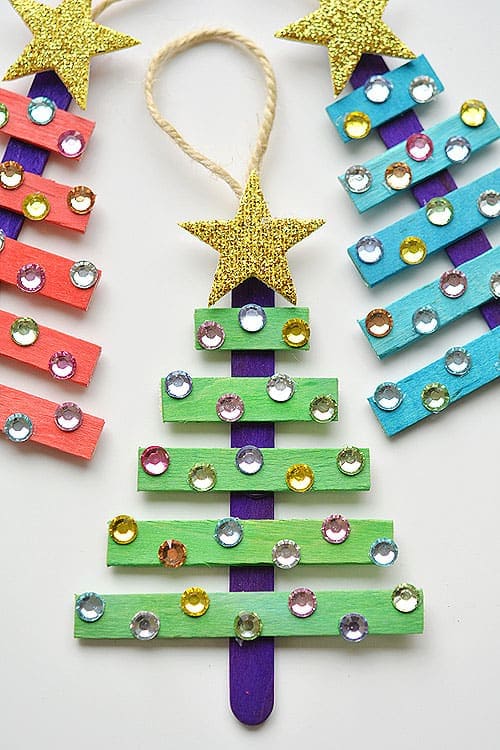 Colorful handmade Christmas tree ornaments made from painted craft sticks capture cherished holiday memories. Each tree is decorated with multicolored gemstones, topped with a glittery gold star, and features a loop of twine for easy hanging—a perfect kid-friendly crafting adventure!