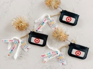 Three Target gift cards, perfect as an end of year teacher gift, are each attached to a small black pouch with a red Target logo on a marble surface. Gold pom-poms and colorful striped tags complete the festive display.